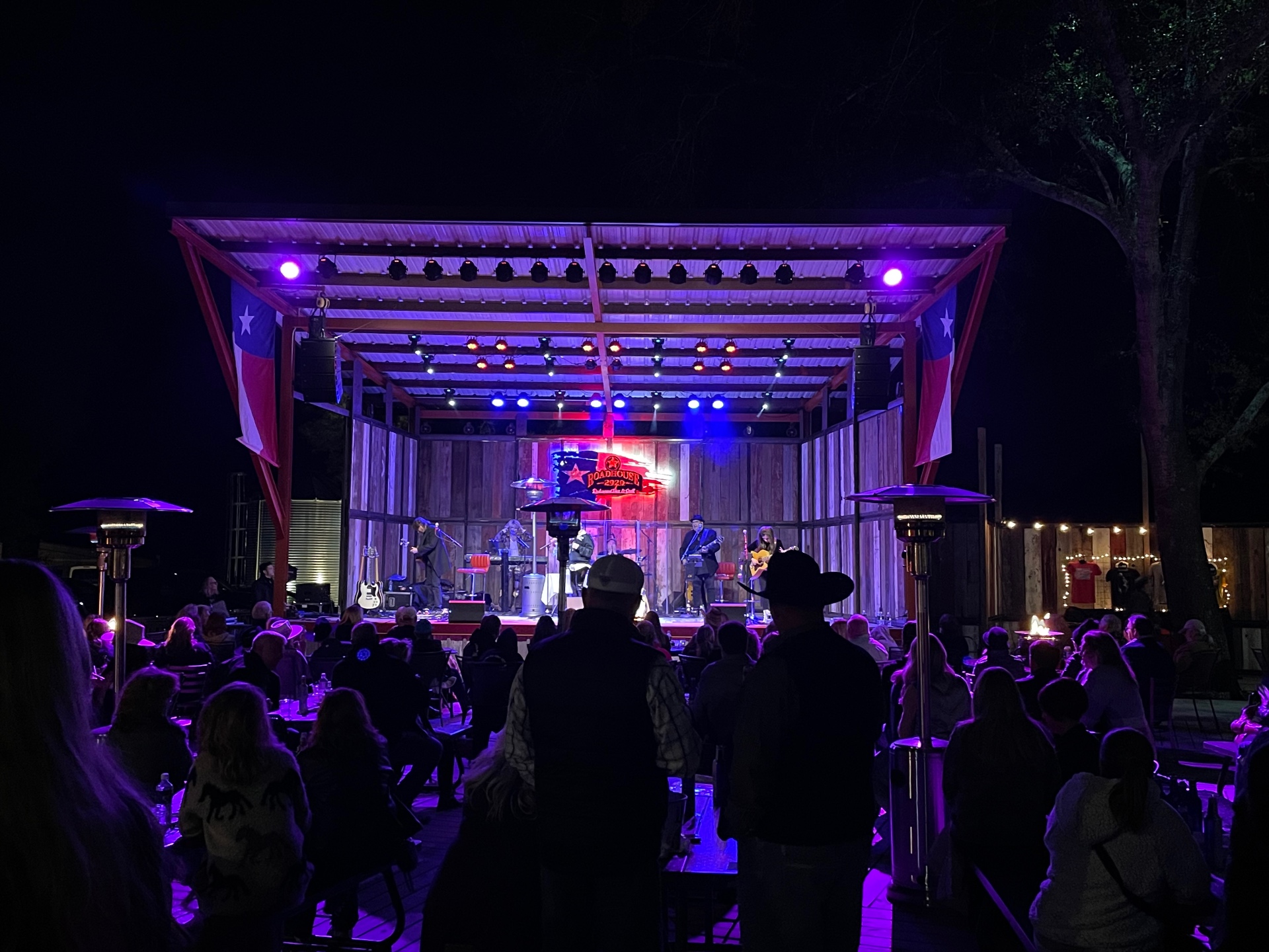 Outdoor roadhouse stage with full lighting rig, line array, and live band under purple wash